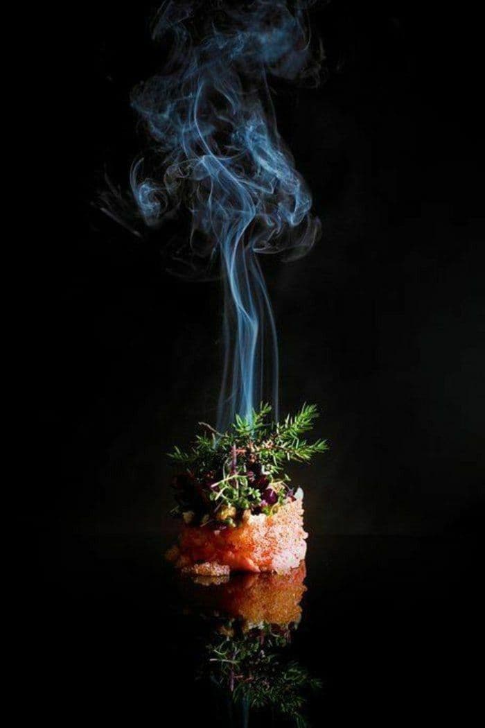 Smoked gourmet appetizer topped with rosemary and microgreens, with blue smoke rising against black.
