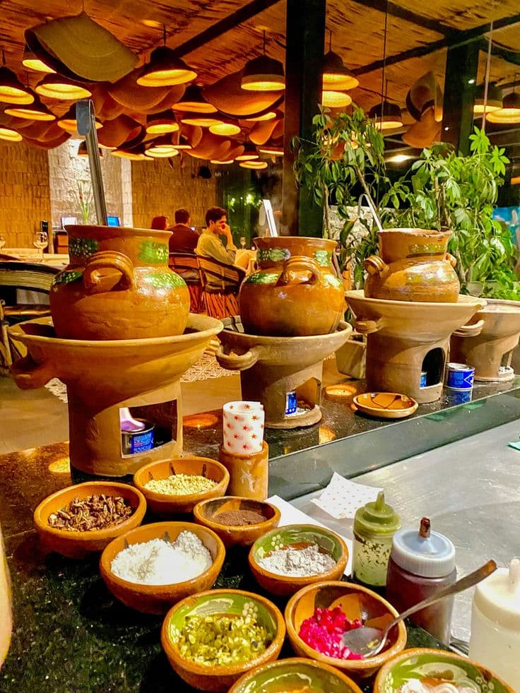 Traditional clay pots on burners and various condiment bowls in a warmly lit restaurant.