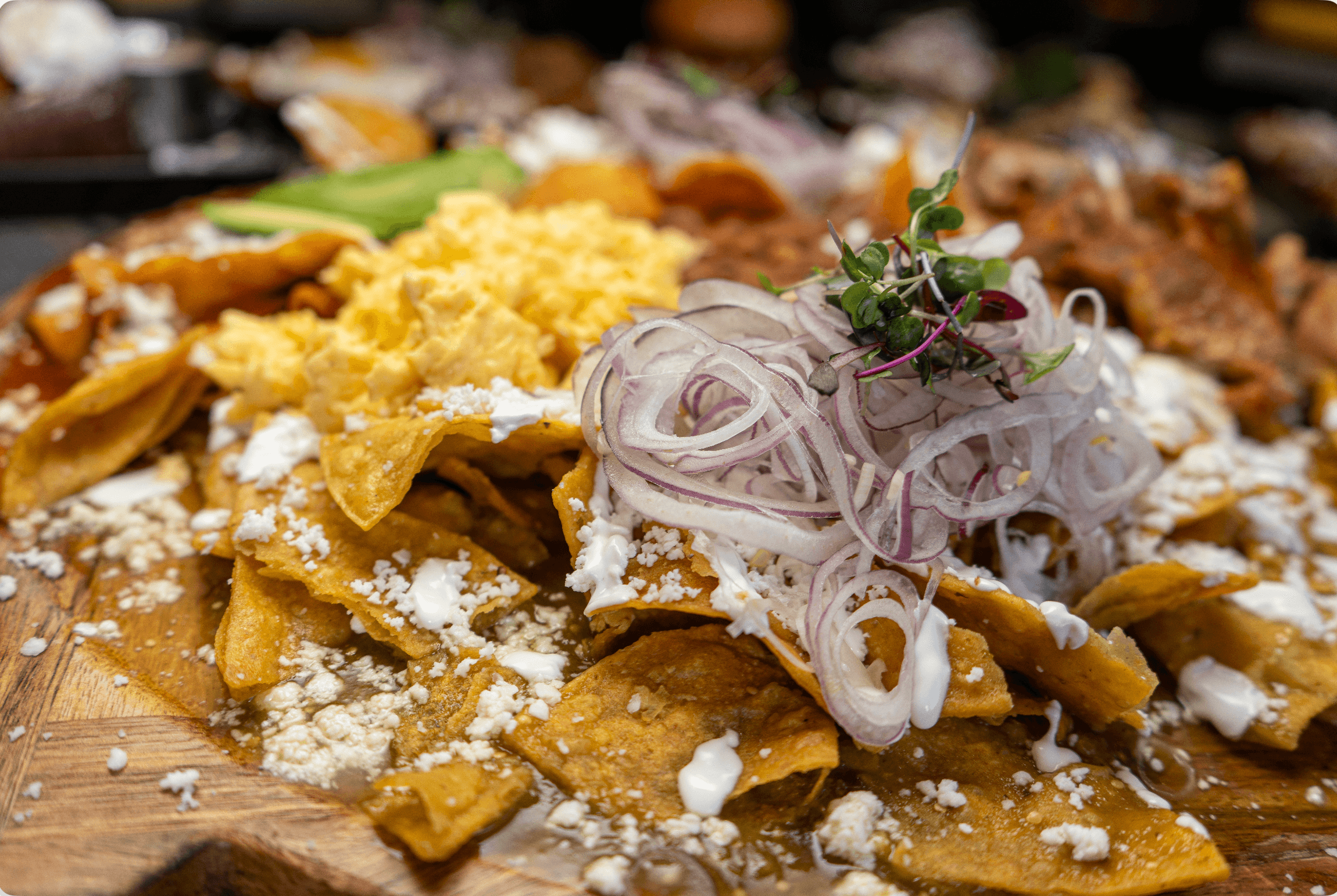Chilaquiles with green salsa, scrambled eggs, red onions, and crumbled cheese on a wooden platter.