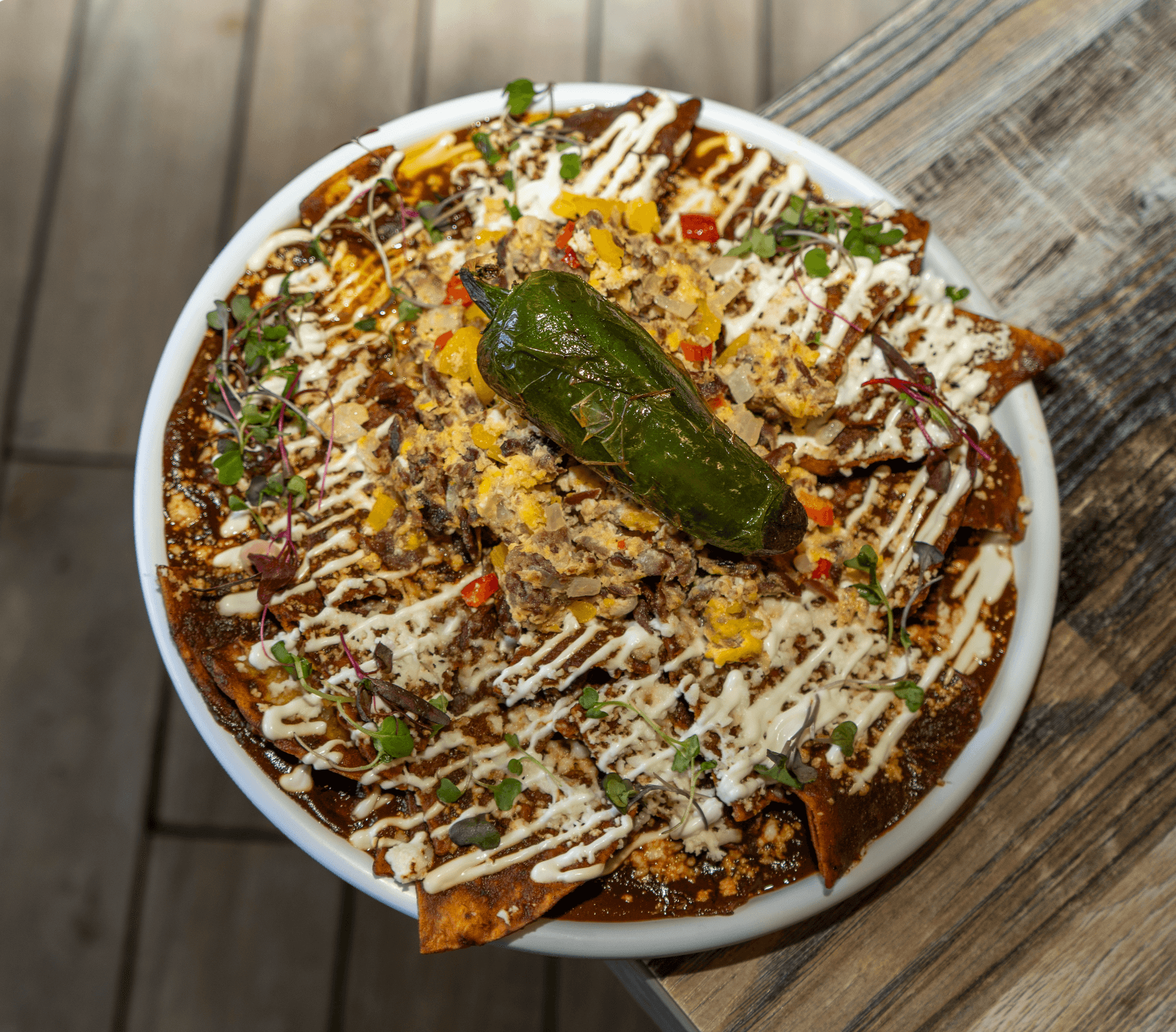Chilaquiles topped with mole, crema, microgreens, and a whole roasted jalapeño on a white plate.