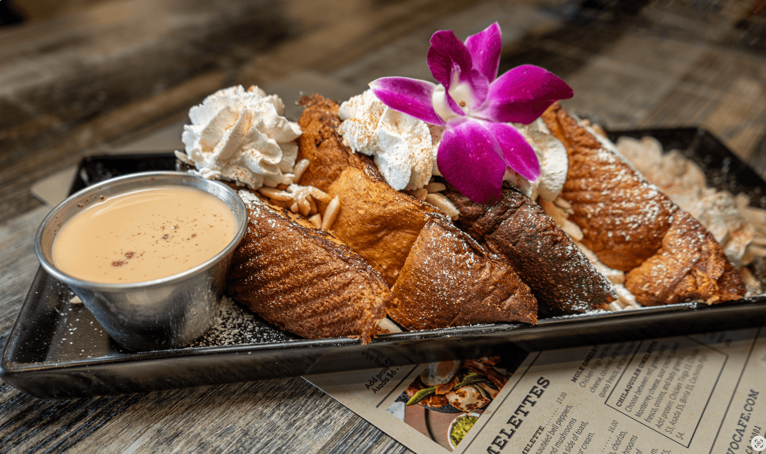French toast topped with whipped cream, almonds, and a purple orchid, served with dipping sauce.