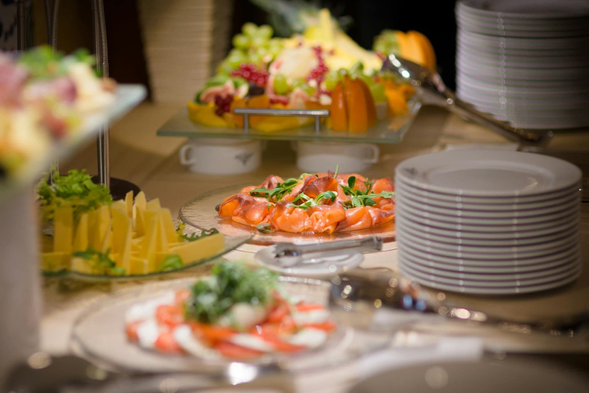 Buffet spread with smoked salmon, sliced cheese, caprese salad, and a vibrant fruit platter.